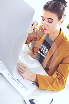 Attractive woman sitting at desk in office, working with laptop computer, holding document