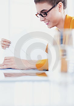 Attractive woman sitting at desk in office, working with laptop computer, holding document