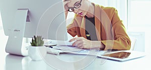 Attractive woman sitting at desk in office, working with laptop computer, holding document