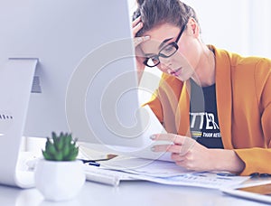 Attractive woman sitting at desk in office, working with laptop computer, holding document