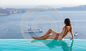 Attractive woman sitting at the edge of an infinity pool and watching the scenery