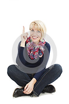 Attractive woman sitting on floor pointing up, looking at camera. Isolated over white background.