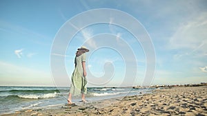 Attractive woman in slow motion walking barefoot along the beach in the early morning. Tourist in a light green dress on