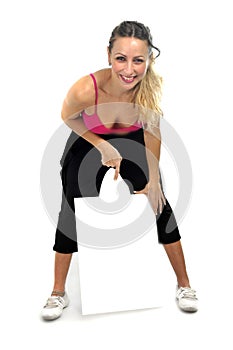 attractive woman in sport pants and gym bra holding and pointing blank billboard card with copy space