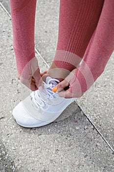 Attractive woman in sportswear tying sport shoes snickers. Concept of fashionable sport outfit, vertical photo. The concept of