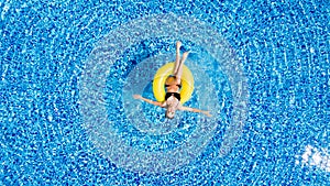 Attractive woman in swimsuit in the yellow rubber ring in the swimming pool from above