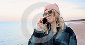 attractive woman talking on mobile phone while walking on the beach coast on chilly day