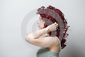 Attractive woman touching her red curly hair against white wall background