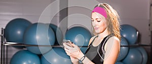 Attractive woman using cell phone and fitness tracker in gym