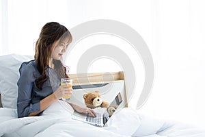 An attractive woman is using her laptop on her bed while drink orange juice