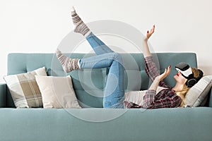 Attractive woman wearing virtual reality glasses lying on a couch. Virtual reality headset. Lifestyle virtual reality