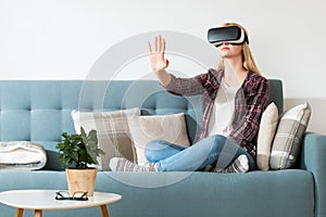 Attractive woman wearing virtual reality glasses sitting on a couch. Virtual reality headset. Lifestyle virtual reality