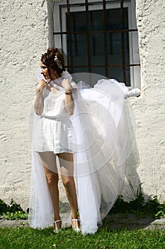 Attractive woman wearing white dress and veil against white wall with barred window