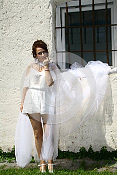 Attractive woman wearing white dress and veil against white wall with barred window