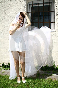 Attractive woman wearing white dress and veil against white wall with barred window
