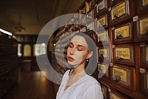 Attractive woman in a white blouse poses for the camera with her eyes closed in the old library archive