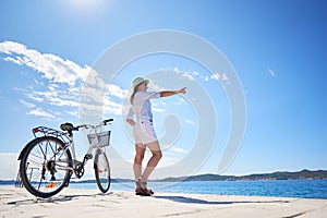 Woman riding a bicycle along stony sidewalk on blue sparkling sea water