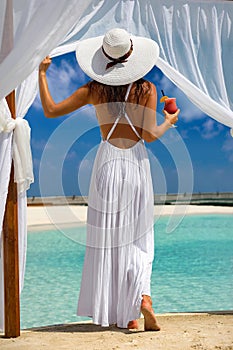 Woman enjoys the view to a tropical beach with a drink in her hand