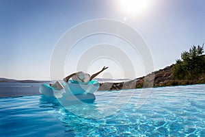 Woman enjoys the view to the Mediterranean sea floating on a infinity pool