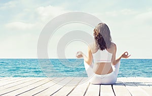 Attractive woman in white sporty clothes doing yoga on a wooden