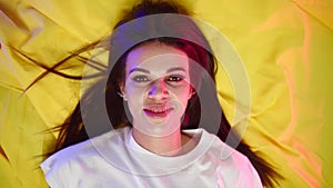 Attractive woman in white t-shirt lies on yellow cloth and smiles seductively