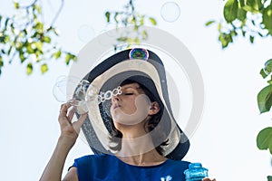 Attractive woman in a wide brimmed sunhat blowing bubbles