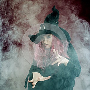 Attractive woman in witches hat with red hair performs magic. Smoke and witchcraft