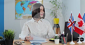 Attractive woman works in a travel agency, on laptop computer, sitting at a table on the background of a world map