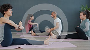 Attractive women and man doing yoga in class stretching legs sitting on mats