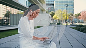 Attractive writer typing laptop sitting urban bench closeup. Woman using earbuds