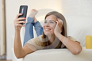 Attractive 30 years old woman playing on home sofa couch taking selfie portrait with mobile phone