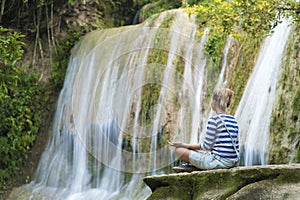 Attractive youn woman during meditation near the waterfall