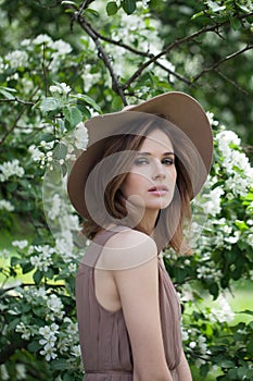 Attractive young adult woman female model with clean fresh skin, make-up and brown hair in blossom garden on green leaves