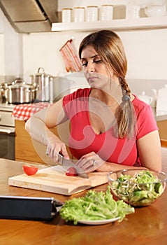 Attractive young adult woman prepares a salad using a digital tablet to read a recipe on the Internet