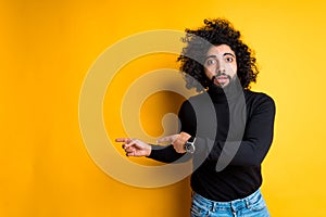 Attractive young african american guy worriedly points fingers to the side while standing on yellow background