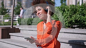 Attractive young african american woman listening to music in headphone use smartphone at city summer sunny day