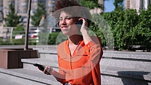 Attractive young african american woman listening to music in headphone use smartphone at city summer sunny day