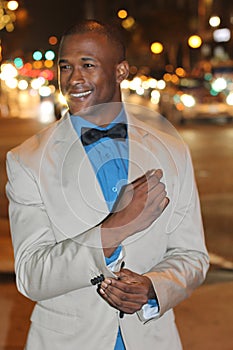 Attractive young African man at night with city lights behind him, wearing elegant suit jacket and bowtie