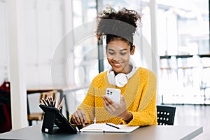 Attractive young African student studying at the college library, sitting at the desk, using a laptop computer, tablet and