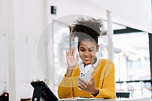 Attractive young African student studying at the college library, sitting at the desk, using a laptop computer, tablet and