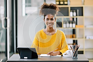 Attractive young African student studying at the college library, sitting at the desk, using a laptop computer, tablet and