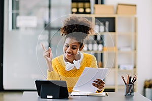 Attractive young African student studying at the college library, sitting at the desk, using a laptop computer, tablet and