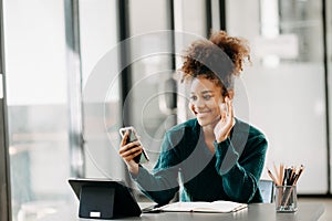 Attractive young African student studying at the college library, sitting at the desk, using a laptop computer, tablet and