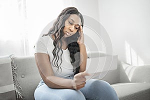 Attractive young African woman sitting on the couch at home stress with bill to pay