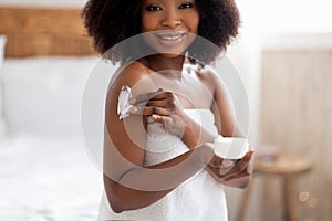 Attractive young Afro woman applying cream on body, pampering herself after bath or shower at home