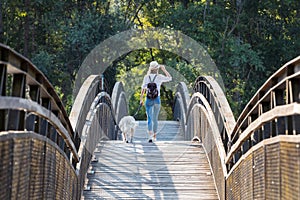 Attractive young amateur photograph woman walking with her dog crossing over a bridge in the park