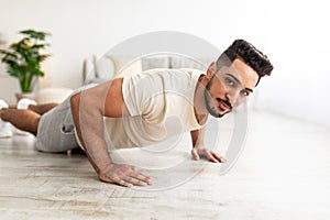Attractive young Arab man standing in plank pose or doing push ups on mat at home