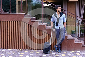 Attractive young Arabic man standing with suitcase in hand and p