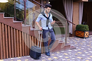 Attractive young Arabic man standing with suitcase in hand and p