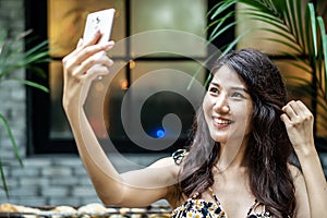 Attractive young asian business woman sitting in cafe and using mobile smartphone selfie happy smiley